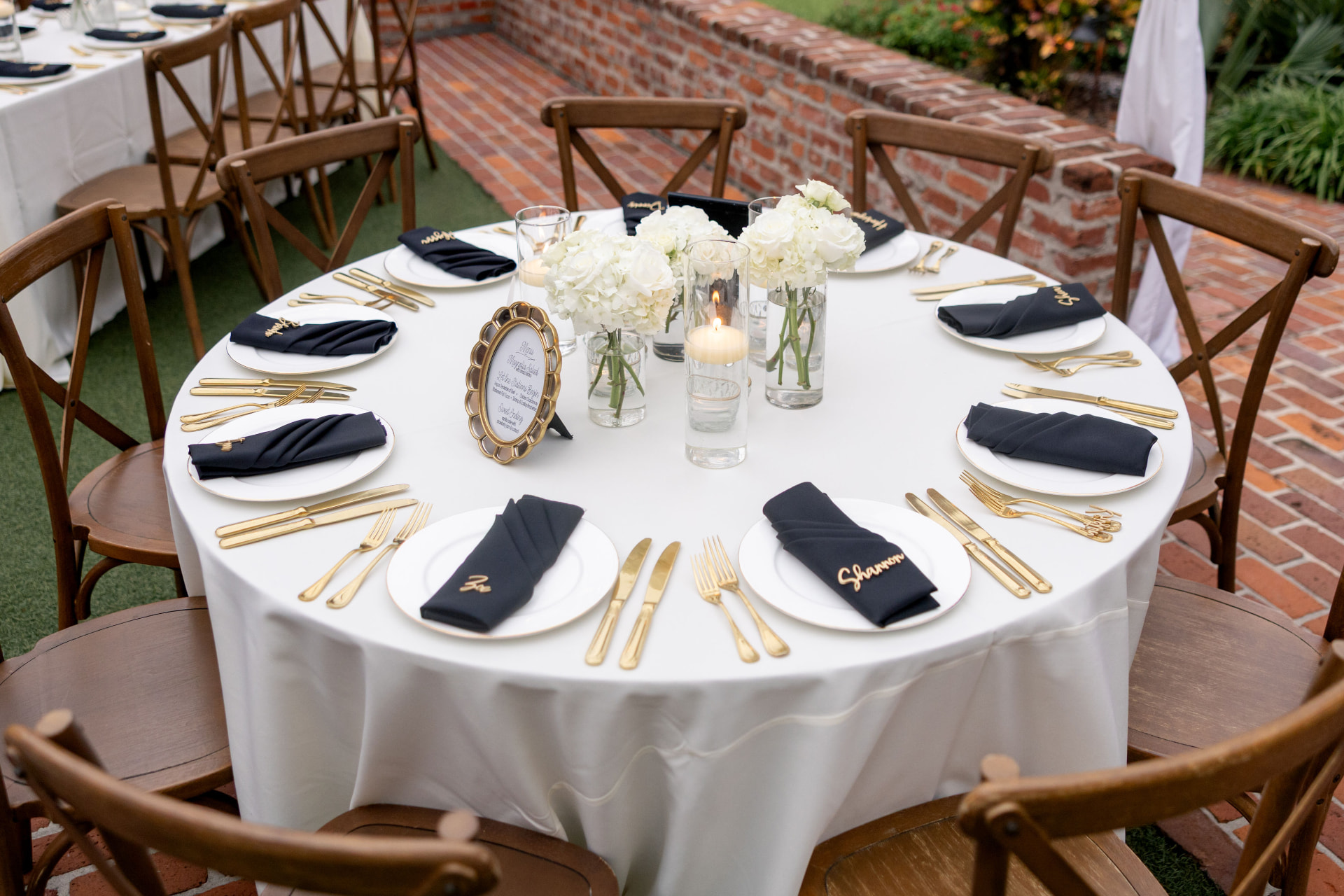 Round table set with cross-back chairs, black linens and gold flatware