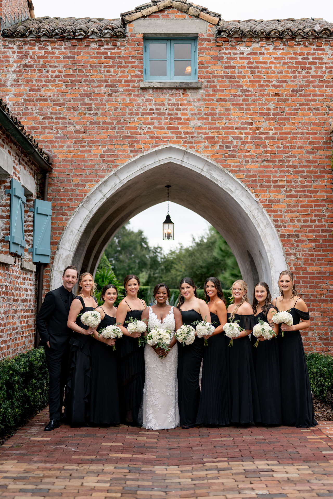 Bride in white surrounded by her bridal party beneath a brick arch
